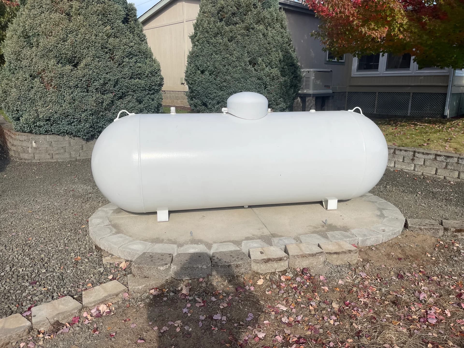 Residential propane tank on stone pad with autumn foliage